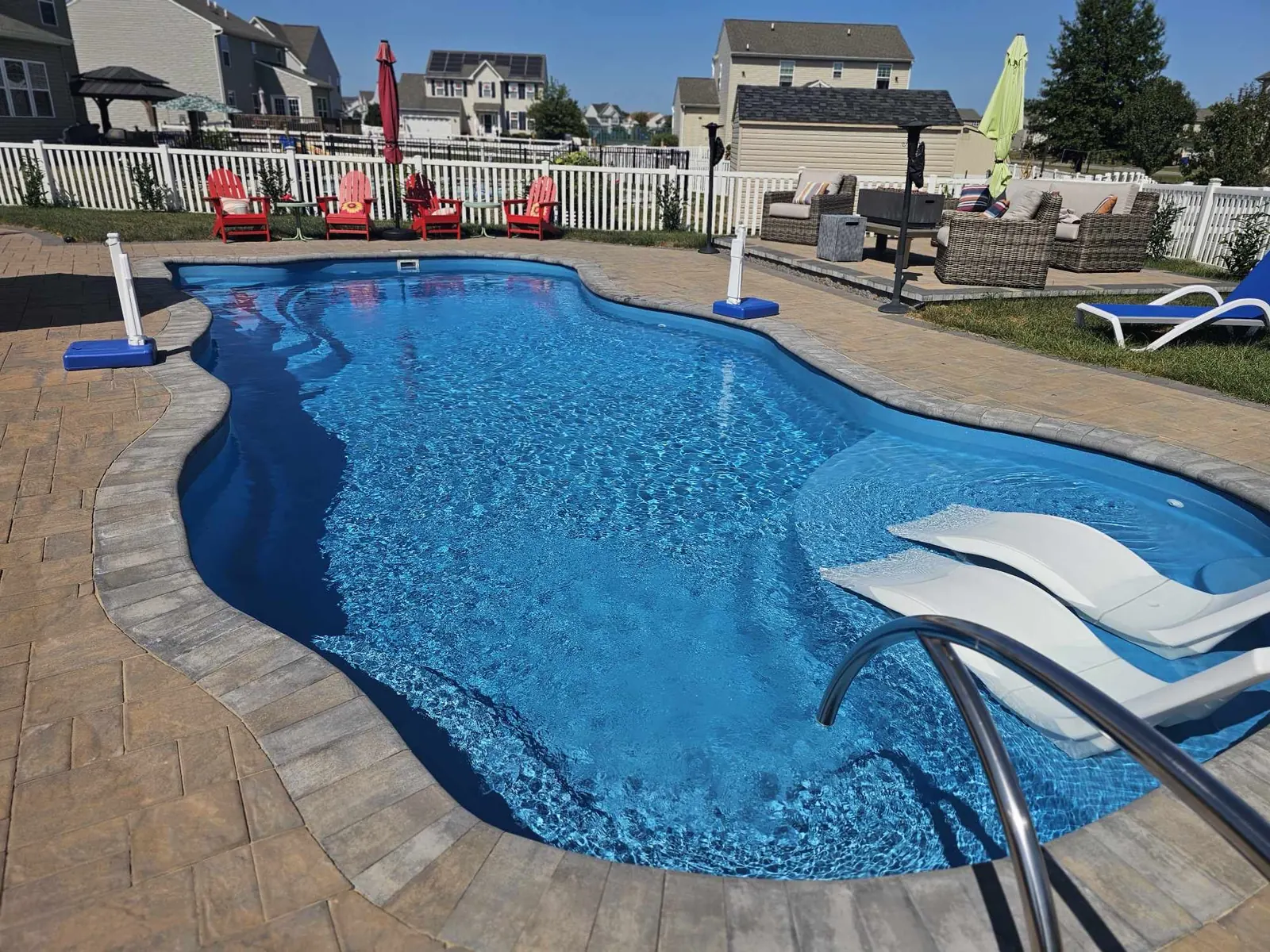 Freeform composite fiberglass pool with a diving board and a sun deck in a backyard